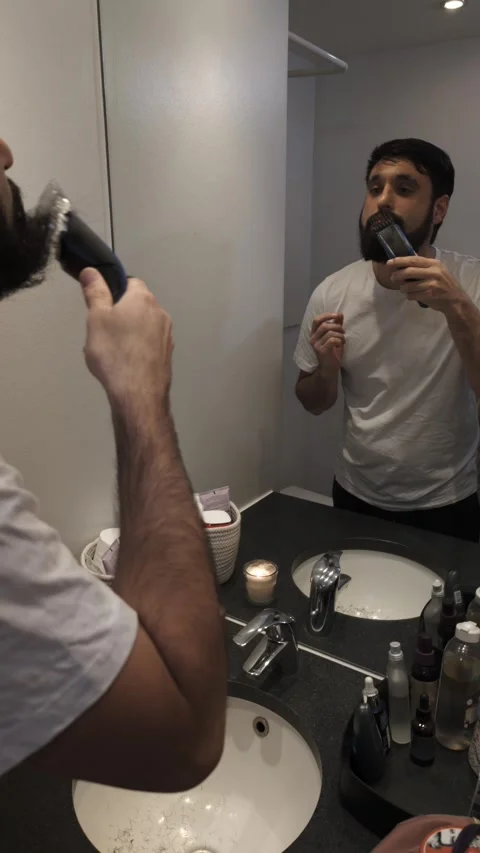 Young bearded man using electric trimmer for daily grooming routine Video stock 335637283