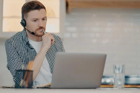 Young bearded man using headset and laptop while working at home Stock Photos