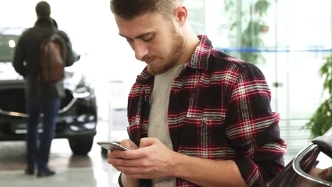 Young bearded man using his smart phone at the car dealership Stock Footage 84929671
