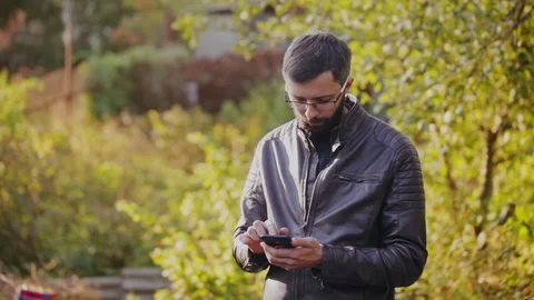 Young bearded man using phone in sunny park Stock Footage 95960361