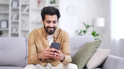 Young bearded man using smartphone sitting on sofa in living room at home.  Stock Footage 252201257