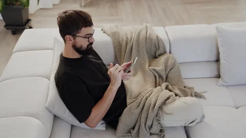 Young bearded man using smartphone on sofa in Stock Footage 260074675
