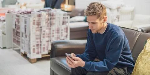 Young bearded man using smartphone sitting on the couch Stock Photos