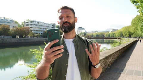 Young bearded man video calling with smartphone outdoors Stock Footage 344820256