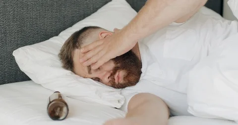 Young bearded man waking up while lying in bed with empty bottle near his head 動画素材 127185026