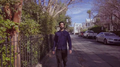 Young bearded man walking down the street along hedge Stock Footage 105313673