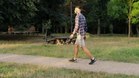 Young bearded man walks alone along a park path on a bright early morning. The Stock Footage 343878886