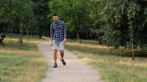 Young bearded man walks alone along a park path on a bright early morning. The Stock Footage 343878963