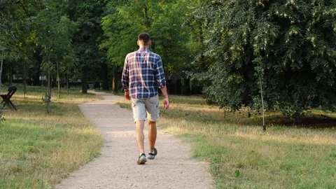 Young bearded man walks alone along a park path on a bright early morning. The Stock Footage 343879024