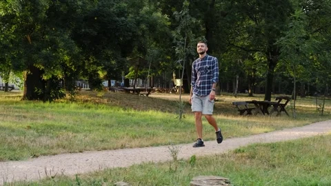 Young bearded man walks alone along a park path on a bright early morning. The Stock Footage 343879326