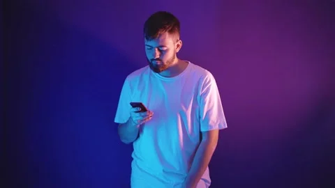 Young bearded man in a white t-shirt holds a smartphone in his hands 库存影片 144342181