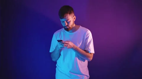 Young bearded man in a white t-shirt holds a smartphone in his hands 库存影片 144605095