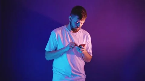 Young bearded man in a white t-shirt holds a smartphone in his hands Vidéo 144673466