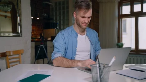 Young bearded man is working with laptop at table in apartment during quarantine Stock Footage 130141147