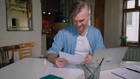 Young bearded man is working with laptop and documents at desk in home during Stock Footage 130192064