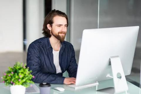 Young bearded man working at xomputer in modern office Stock Photos