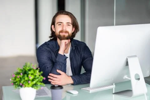 Young bearded man working at xomputer in modern office Stock Photos