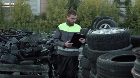 A young bearded mechanic in uniform checks tires stacked in rows in the yard of Stock Footage 137598618
