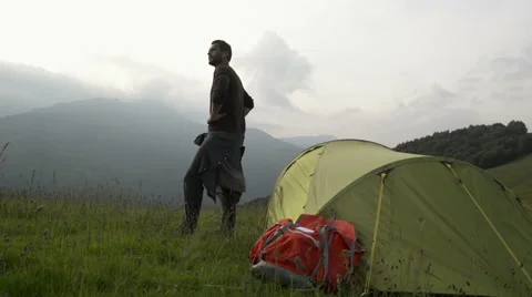 Young beautiful beard man on mountain is watching panorama near his tent 動画素材 64516269