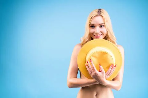 Young beautiful blond woman is covering her body with yellow hat. Ready for b Stock Photos