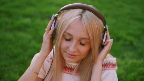 Young beautiful blonde listening to music with headphones in the park on sunset Stock Footage