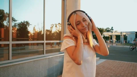 Young beautiful blonde listening to music with headphones in the urban city on Stock Footage