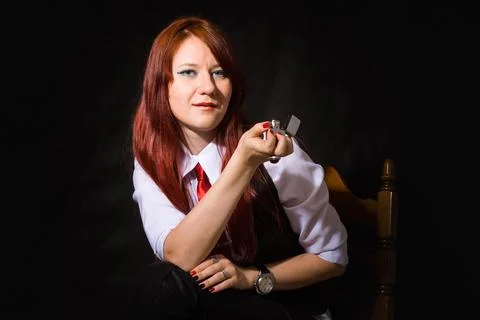 A young beautiful bold red-haired girl is sitting on a chair with a lighter. Stock Photos