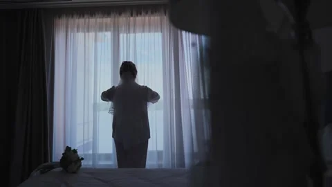 A young beautiful bride opens the curtains Vídeos de archivo 327983336