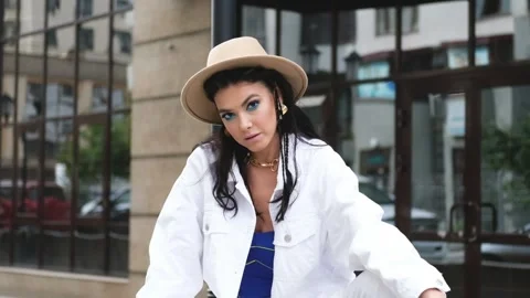 Young beautiful brunette in a white jacket and brown hat sits on the background Stock-Footage 164920486