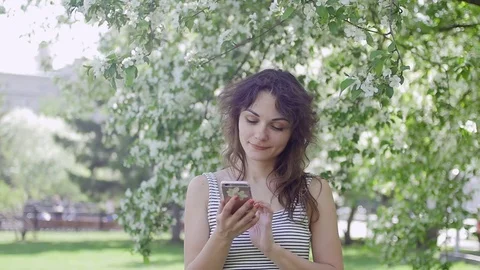 Young beautiful brunette woman is talking on the phone in the Park Stock Footage
