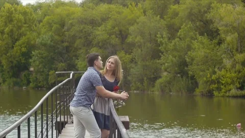 Young beautiful couple on a date standing on a bridge by the lake Stock Footage