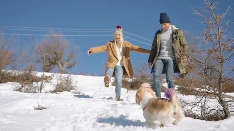 Young beautiful couple having fun with small active dog on a snowy hill Stock Footage 124878322