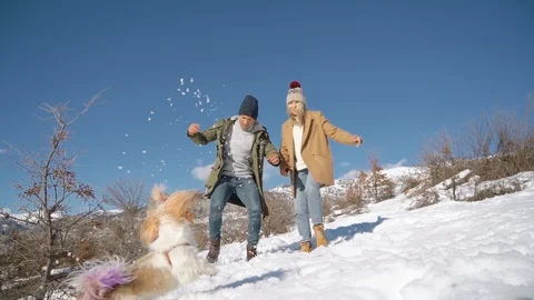 Young beautiful couple having fun with small active dog on a snowy hill Stock Footage 125055328
