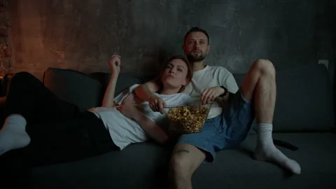 A young beautiful couple is lying on the couch and watching TV Stock Footage 197780948