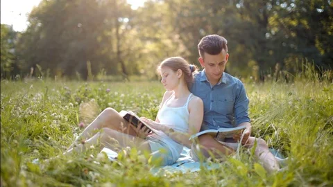 Young Beautiful Couple Reading Books Outdoors in Summer, Smiling and Kissing Stock Footage