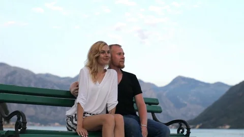 Young beautiful couple resting on a bench on a background of mountains and lake Stock Footage 92143122