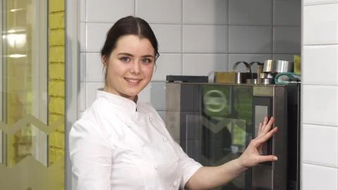 Young beautiful female confectioner putting merengues into the oven Stock Photos