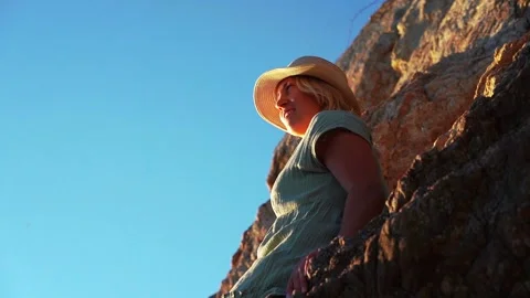 Young beautiful female model in hat standing in sea near huge rock Stock Footage 219378985