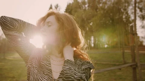 Young beautiful ginger lady playing with her long curly hair. Sunset rays. Stock Footage 124213614