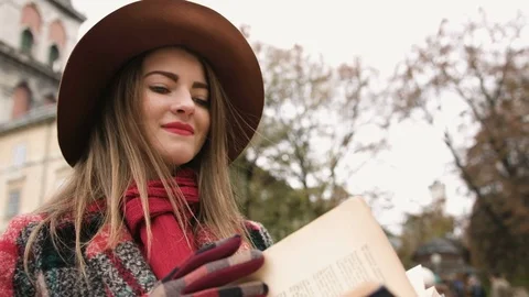Young beautiful girl in hat reading book in city park. Slow motion Stock Footage