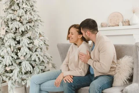 Young beautiful happy couple, sitting on the couch near the Christmas tree. Stock Photos