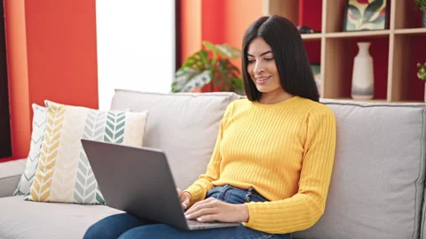 Young beautiful hispanic woman using laptop sitting on sofa at home Stock Footage 236760347