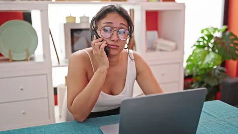 Young beautiful hispanic woman using laptop talking on smartphone looking u.. Video stock 243485089