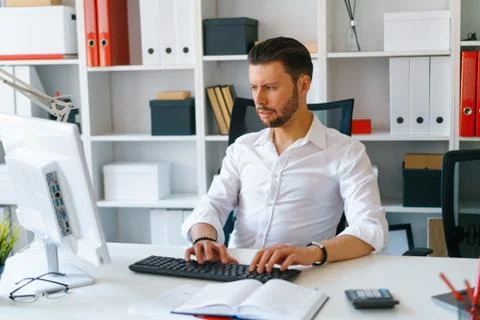 Young beautiful man work on computer sit at table in office smile Stock Photos