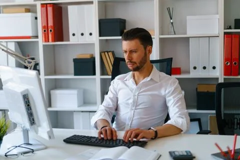 Young beautiful man work on computer sit at table in office smile Stock Photos