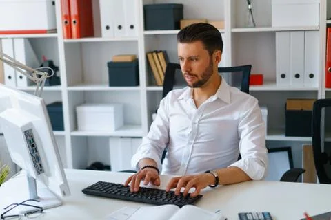 Young beautiful man work on computer sit at table in office smile Stock Photos