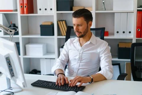 Young beautiful man work on computer sit at table in office smile Stock Photos