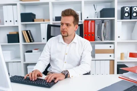Young beautiful man work on computer sit at table in office smile Stock Photos