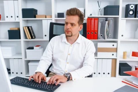Young beautiful man work on computer sit at table in office smile Stock Photos