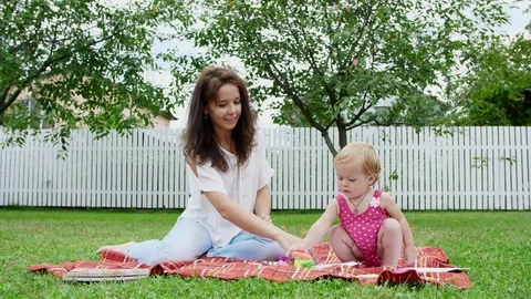 A young beautiful mother playing with a one-year-old daughter, in the garden Stock-Footage 80440334